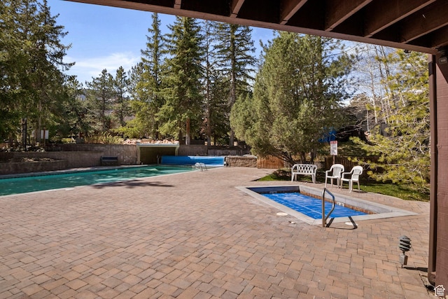 view of pool featuring a patio, view of wooded area, and fence
