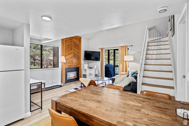 dining space with a fireplace, stairway, light wood finished floors, baseboards, and lofted ceiling