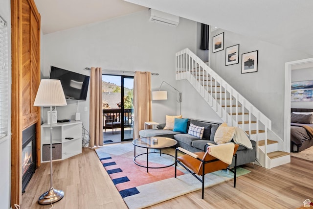 living area with wood finished floors, a wall mounted air conditioner, stairway, high vaulted ceiling, and a glass covered fireplace