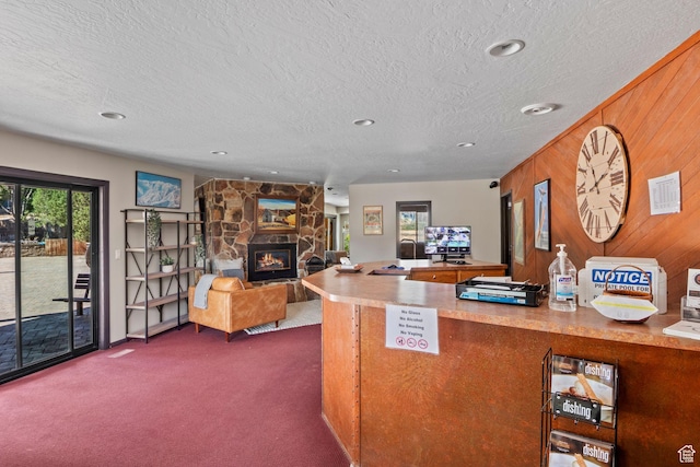 kitchen with dark carpet, a textured ceiling, wooden walls, a stone fireplace, and recessed lighting