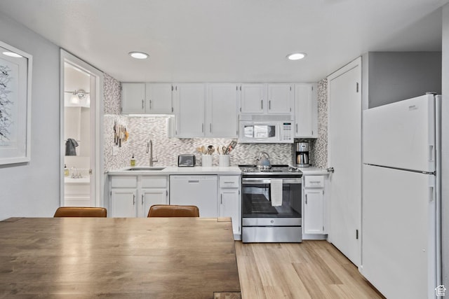 kitchen with white appliances, a sink, white cabinets, and recessed lighting