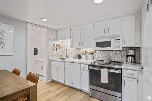 kitchen with white appliances, a sink, white cabinets, light countertops, and recessed lighting