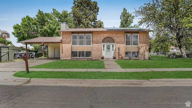 raised ranch with an attached carport, driveway, solar panels, a chimney, and brick siding