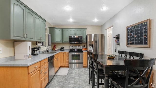 kitchen with stainless steel appliances, a sink, green cabinetry, and light countertops