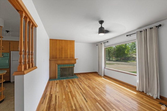unfurnished living room with ceiling fan, a large fireplace, wood finished floors, and baseboards