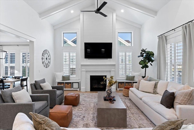living area with high vaulted ceiling, beam ceiling, ceiling fan, a brick fireplace, and wood finished floors