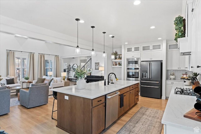 kitchen featuring appliances with stainless steel finishes, a sink, light wood-type flooring, an island with sink, and white cabinetry