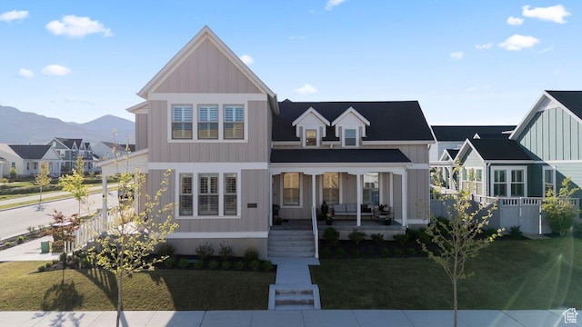 view of front of property with a porch, board and batten siding, a mountain view, a front yard, and a residential view