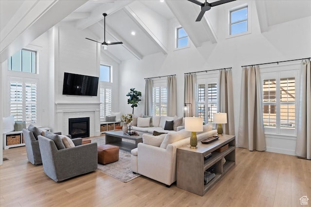 living room with ceiling fan, high vaulted ceiling, beamed ceiling, a fireplace, and light wood-type flooring