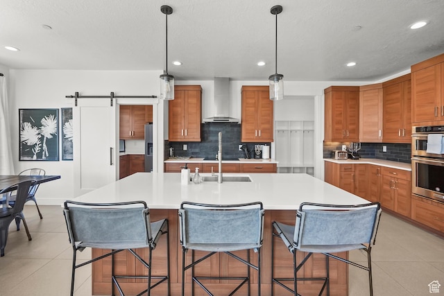 kitchen featuring wall chimney range hood, brown cabinetry, stainless steel double oven, tasteful backsplash, and recessed lighting