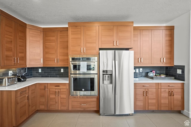 kitchen with appliances with stainless steel finishes, light countertops, backsplash, brown cabinetry, and light tile patterned floors