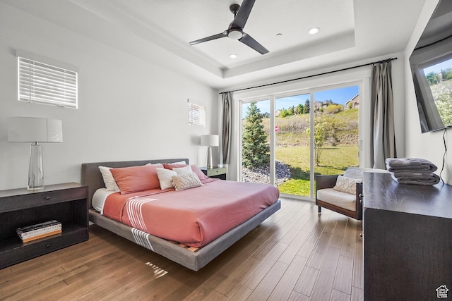 bedroom with a raised ceiling, access to outside, wood finished floors, recessed lighting, and a ceiling fan
