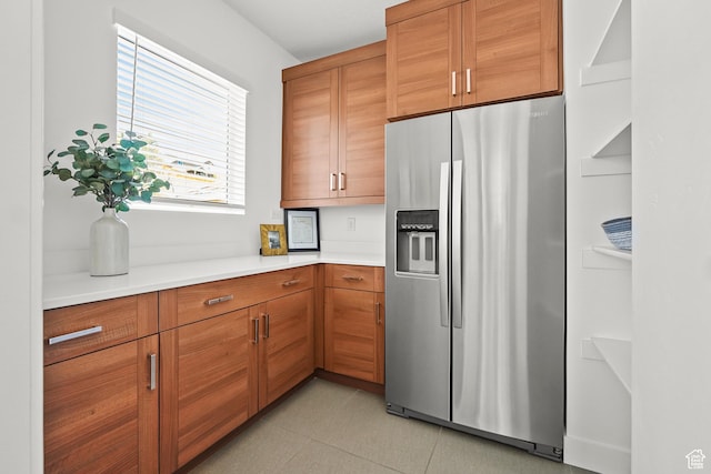 kitchen featuring stainless steel fridge, light countertops, brown cabinets, and light tile patterned floors