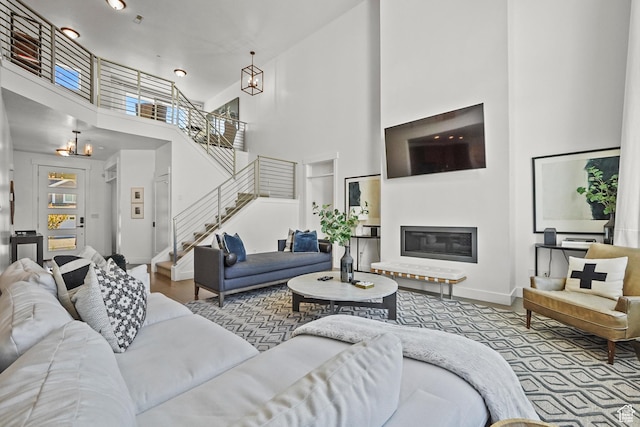 living area with a chandelier, a towering ceiling, stairs, a glass covered fireplace, and baseboards