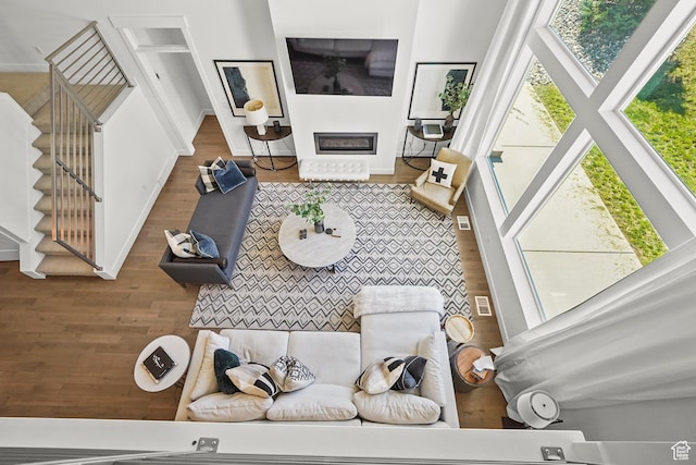 living area with wood finished floors, stairway, a glass covered fireplace, and baseboards