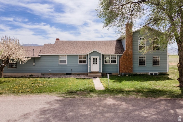 view of front of house featuring a chimney, a front yard, entry steps, and a shingled roof