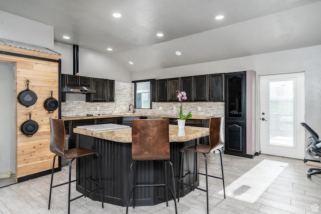 kitchen with a breakfast bar area, tasteful backsplash, vaulted ceiling, a kitchen island, and light wood finished floors