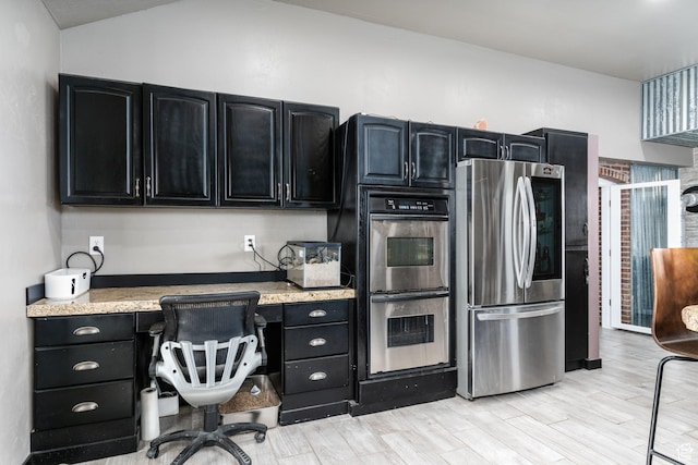 kitchen with appliances with stainless steel finishes, dark cabinets, light wood-type flooring, and lofted ceiling