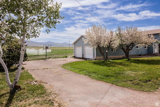 view of side of property featuring asphalt driveway, an attached garage, a yard, and a mountain view