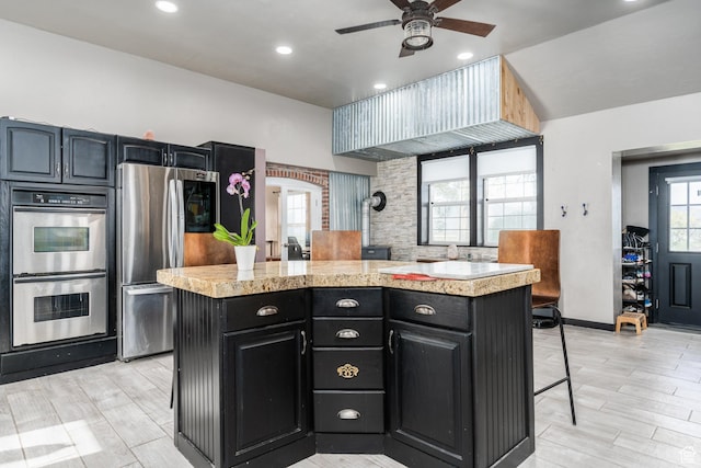 kitchen with appliances with stainless steel finishes, light countertops, a kitchen island, a breakfast bar area, and ceiling fan
