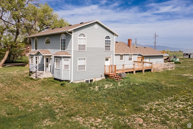 rear view of house with a lawn, roof with shingles, a chimney, and a wooden deck