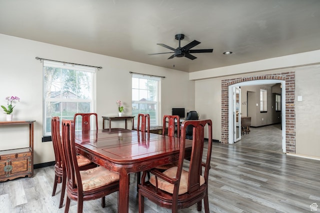 dining room with light wood finished floors, a ceiling fan, arched walkways, and baseboards