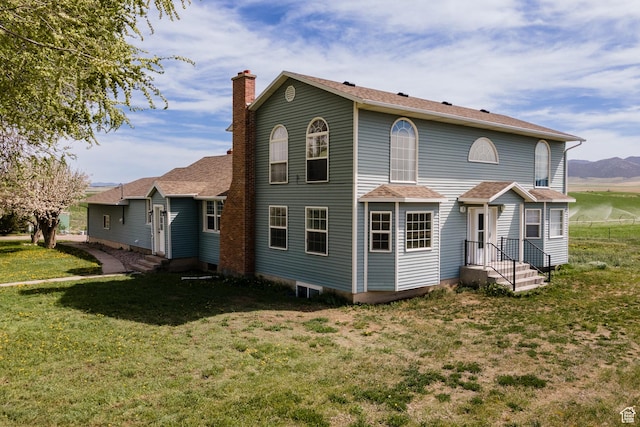 back of house with a lawn, a chimney, and a shingled roof