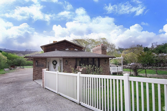 view of front facade featuring a fenced front yard, a chimney, brick siding, and a shingled roof