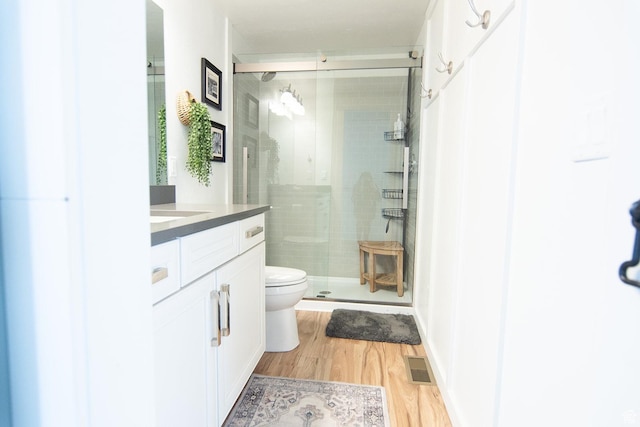 bathroom with wood finished floors, a shower stall, vanity, and toilet