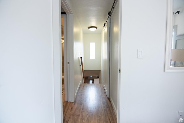 hallway featuring a barn door, wood finished floors, an upstairs landing, and baseboards
