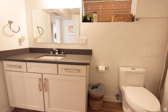 bathroom with toilet, vanity, wood finished floors, and baseboards