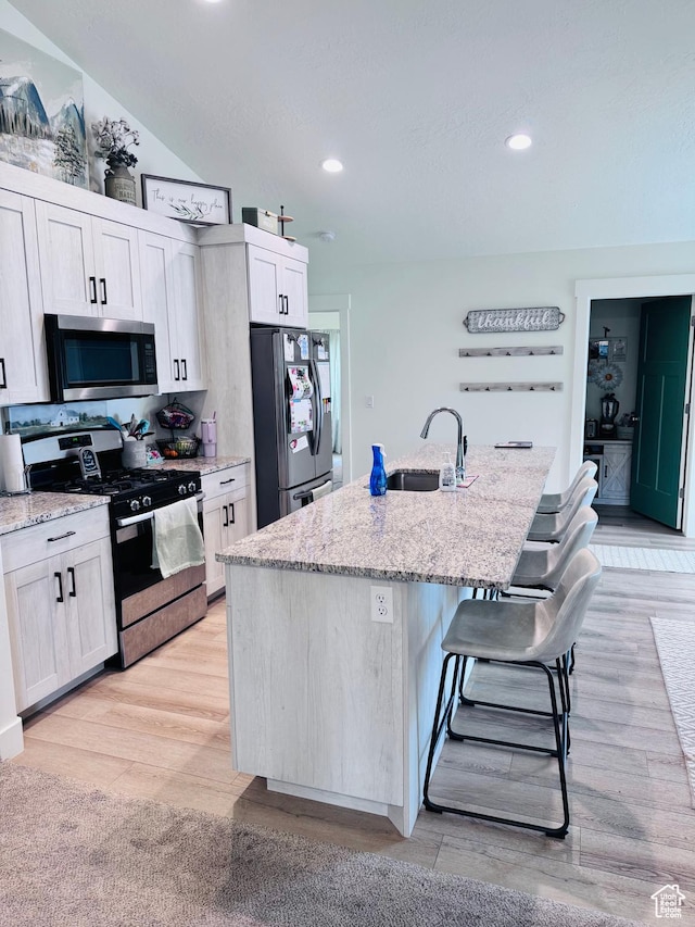 kitchen featuring stainless steel appliances, a sink, a center island with sink, a breakfast bar area, and light wood-style floors