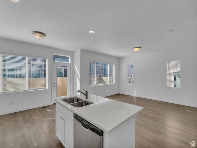 kitchen with stainless steel dishwasher, a sink, wood finished floors, white cabinets, and baseboards