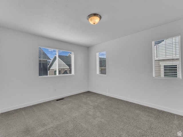 carpeted empty room featuring baseboards and plenty of natural light
