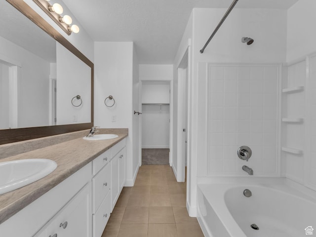 full bath featuring tile patterned flooring, double vanity, baseboards, a walk in closet, and a textured ceiling