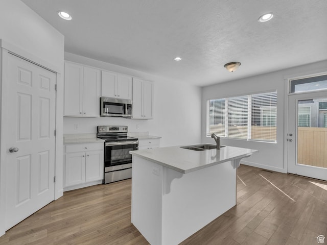 kitchen with appliances with stainless steel finishes, a sink, white cabinets, light wood-type flooring, and recessed lighting