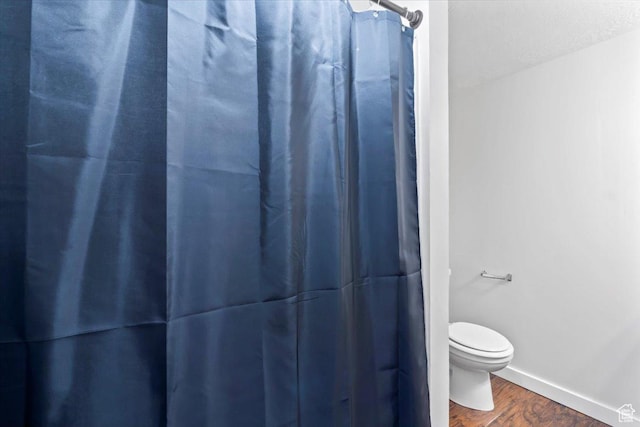 bathroom with wood finished floors, toilet, a shower with shower curtain, and baseboards