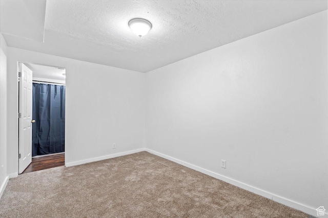 carpeted empty room featuring a textured ceiling and baseboards