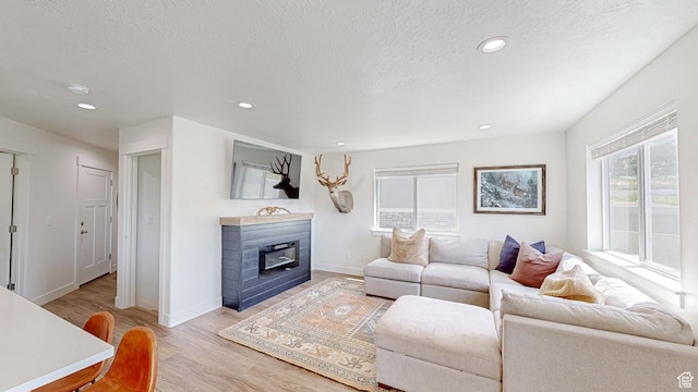 living area with light wood-type flooring, a textured ceiling, recessed lighting, and baseboards