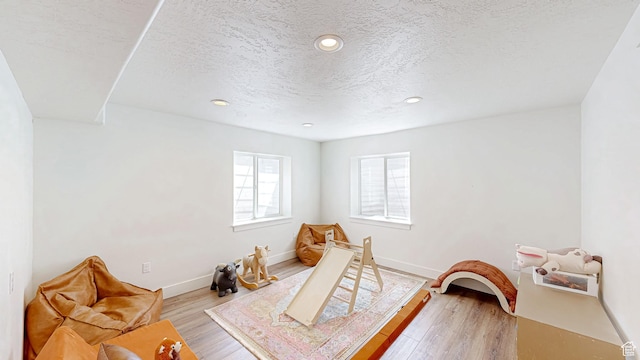 recreation room with a textured ceiling, light wood finished floors, baseboards, and recessed lighting
