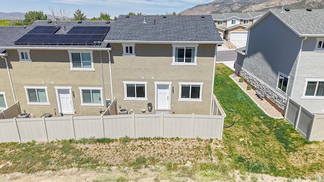 back of house with a mountain view, stucco siding, a shingled roof, and fence