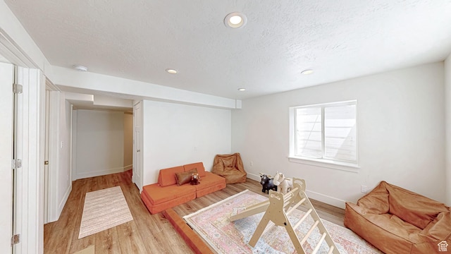 living area with light wood-style floors, a textured ceiling, baseboards, and recessed lighting