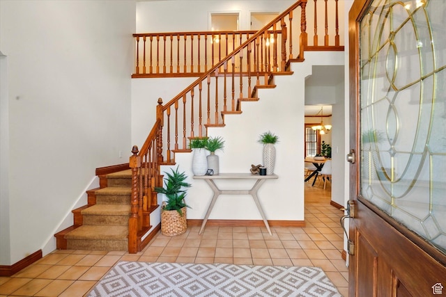 entrance foyer with light tile patterned floors, baseboards, stairway, and a chandelier