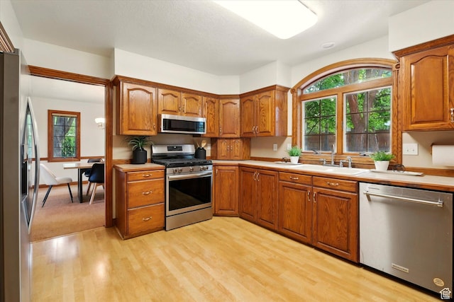kitchen with stainless steel appliances, light wood-type flooring, brown cabinetry, and light countertops