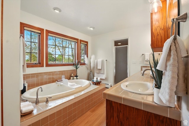 full bath with a baseboard radiator, wood finished floors, a stall shower, a garden tub, and vanity