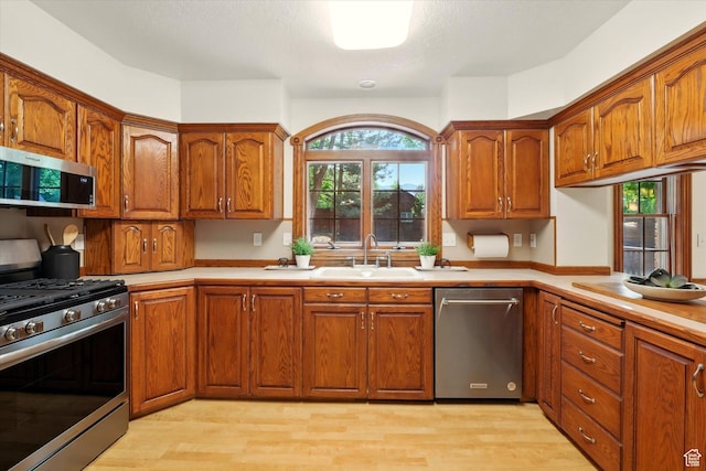 kitchen featuring stainless steel appliances, a sink, light wood-type flooring, and brown cabinets