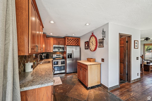 kitchen with stainless steel appliances, a sink, backsplash, baseboards, and brown cabinets