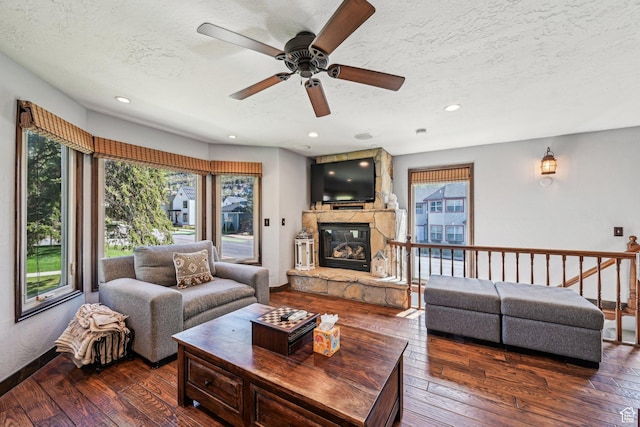 living area featuring a textured ceiling, a stone fireplace, wood-type flooring, ceiling fan, and recessed lighting