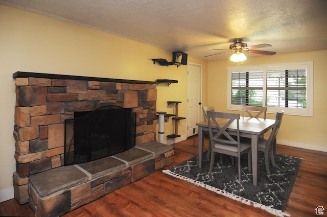 dining space with ceiling fan, wood finished floors, a fireplace, baseboards, and a textured ceiling