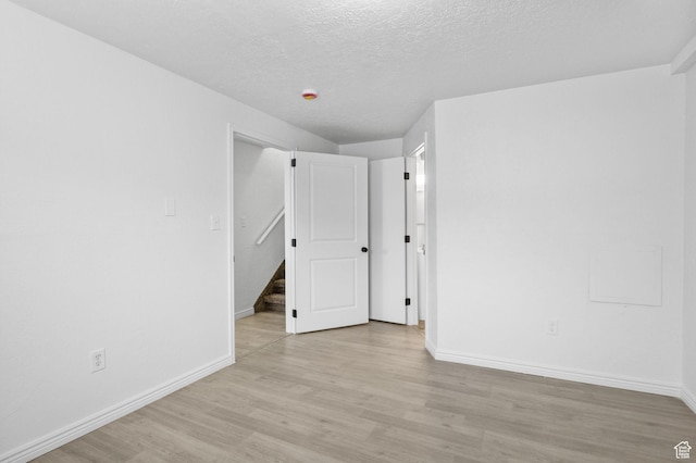 spare room featuring light wood-style flooring, baseboards, and a textured ceiling